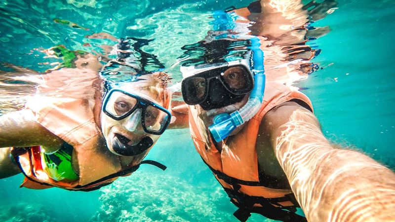 Active senior couple taking under water selfie in tropical sea excursion with water camera -