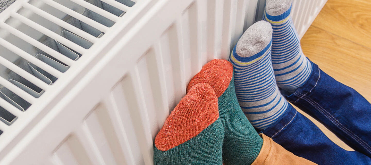 2 pairs of feet with socks on pressing against a radiator