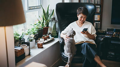 Senior woman using her smartphone at home while stroking her cat
