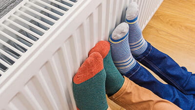 2 pairs of feet with socks on pressing against a radiator