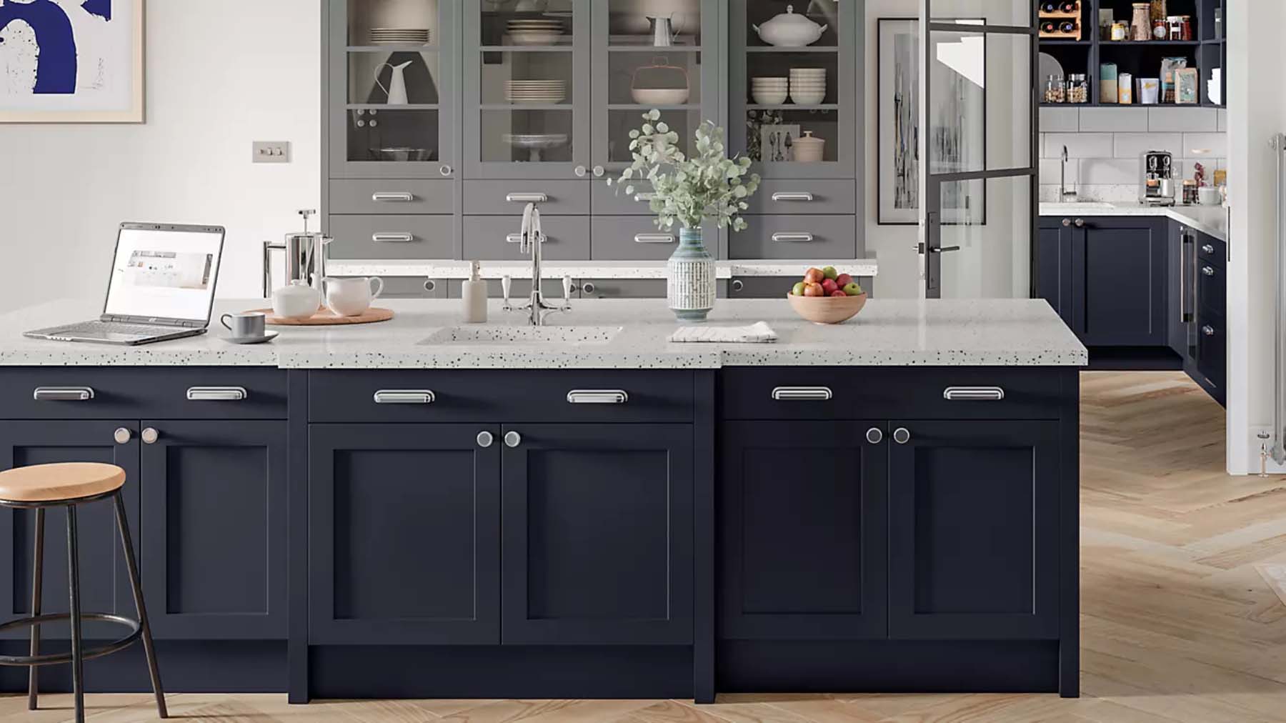 A John Lewis kitchen comprised of a dark, marble-topped island in the foreground and tall grey, glass-fronted cabinets in the background.