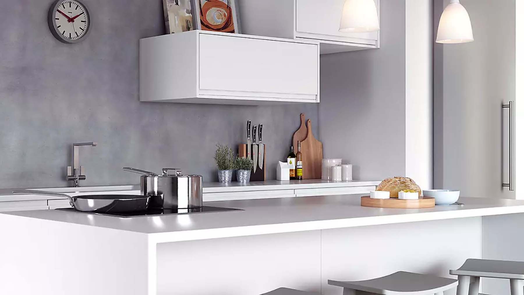 A white kitchen countertop containing a flat hob and silver pans, with white kitchen cupboards visible in the background.