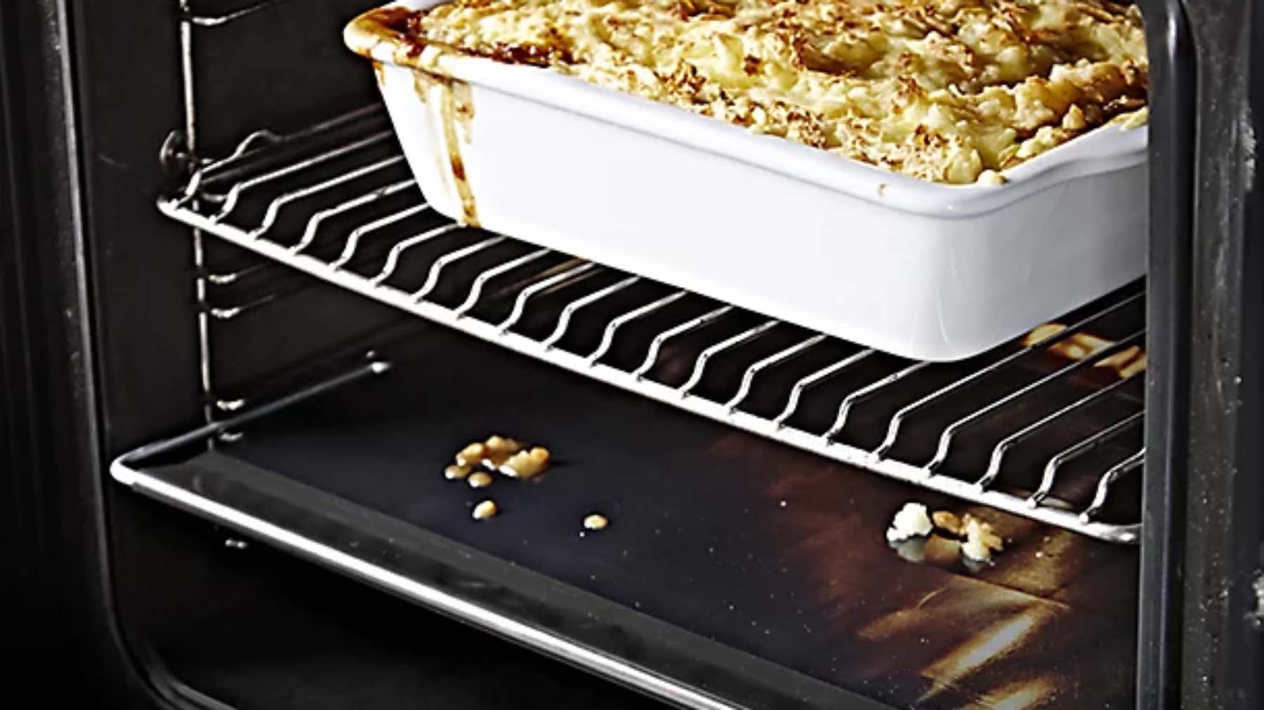 Close-up of a baking dish in the oven with gravy dripping down the side.