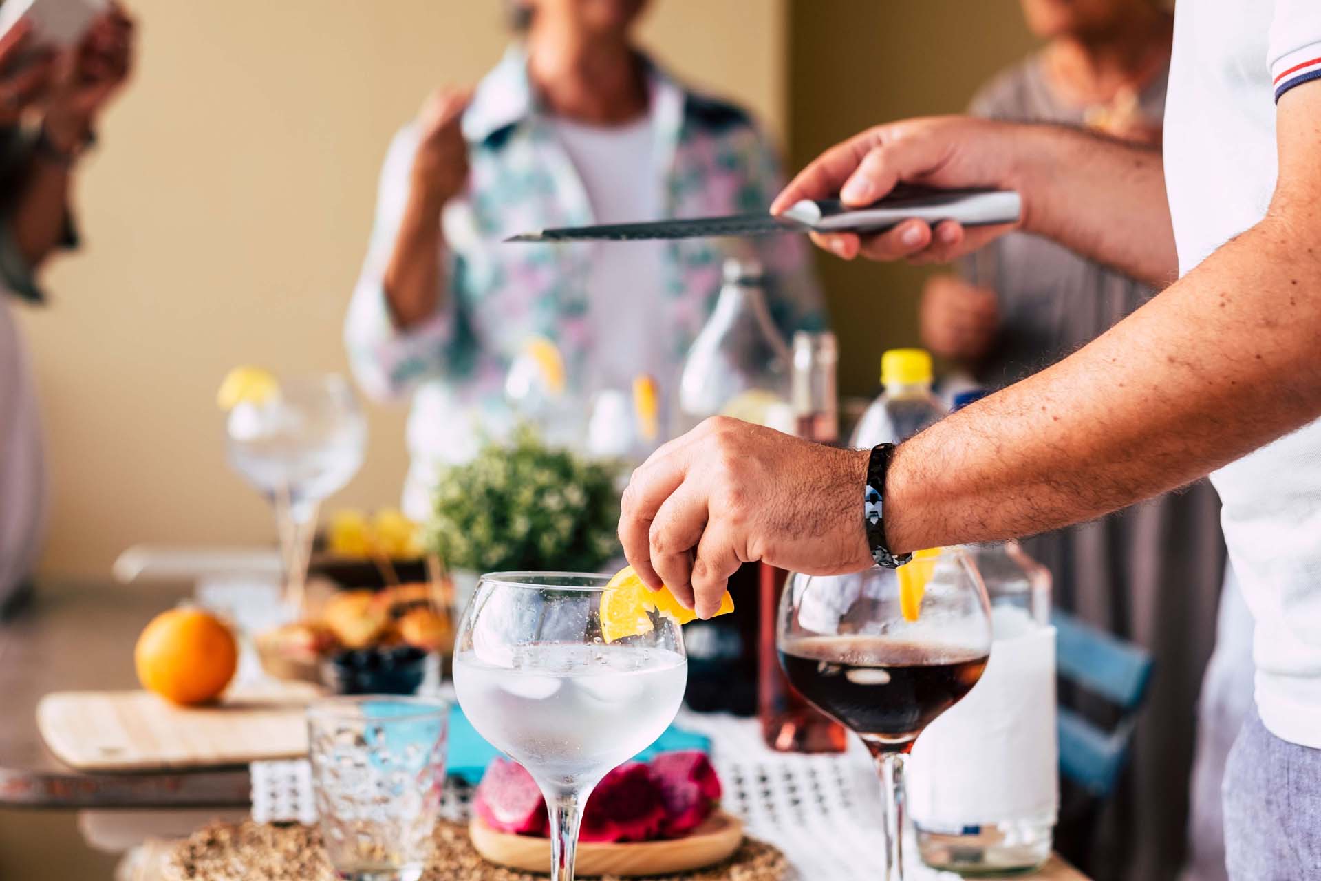Close-up of someone making cocktails with citrus fruit garnishes while entertaining guests