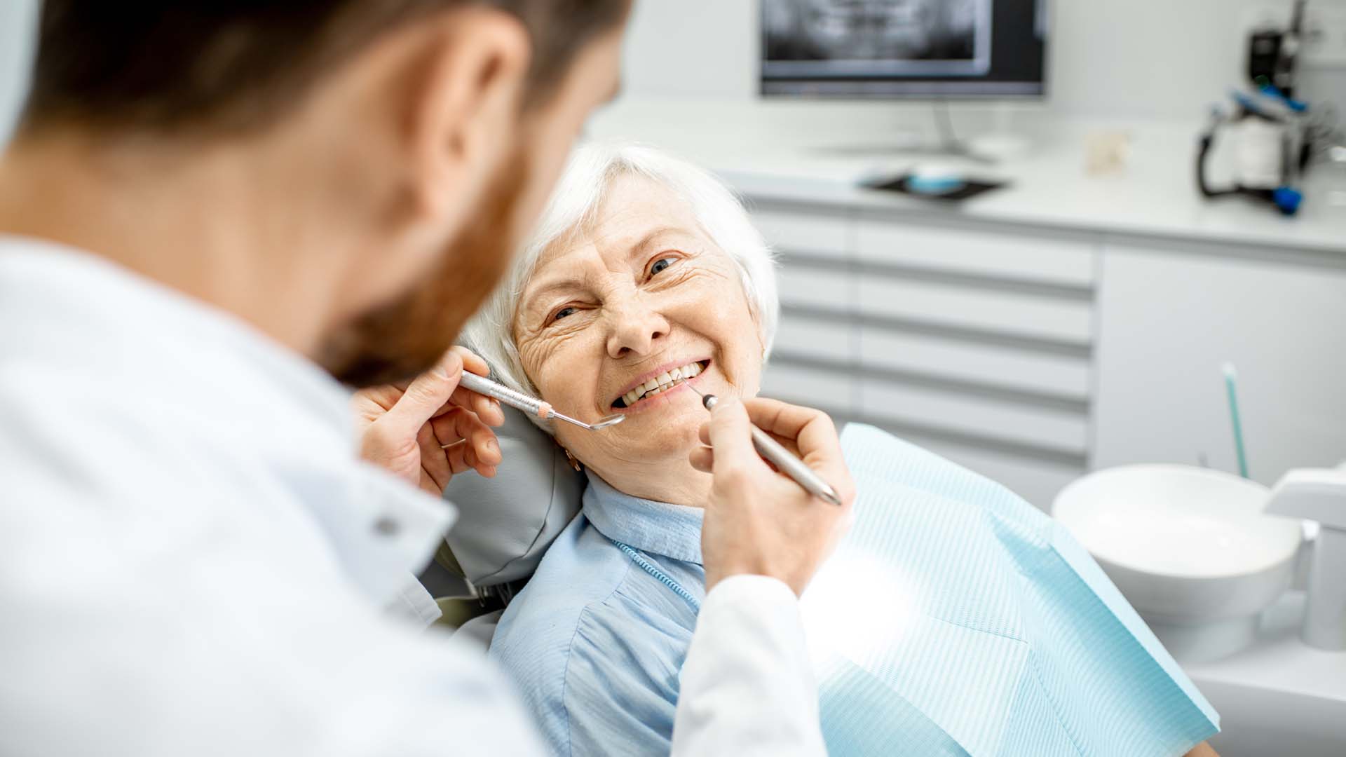 An older woman smiling whilst looking up at her dentist