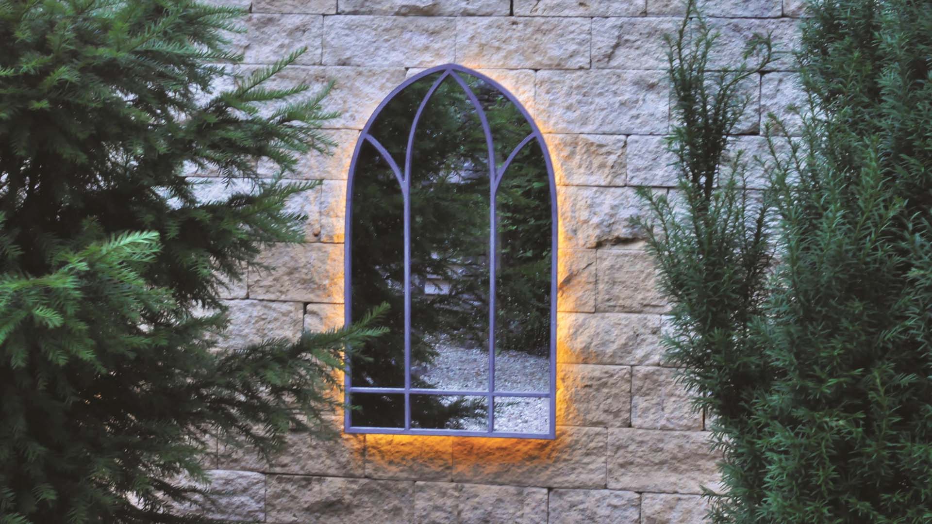 Arched, backlit mirror hanging on garden wall