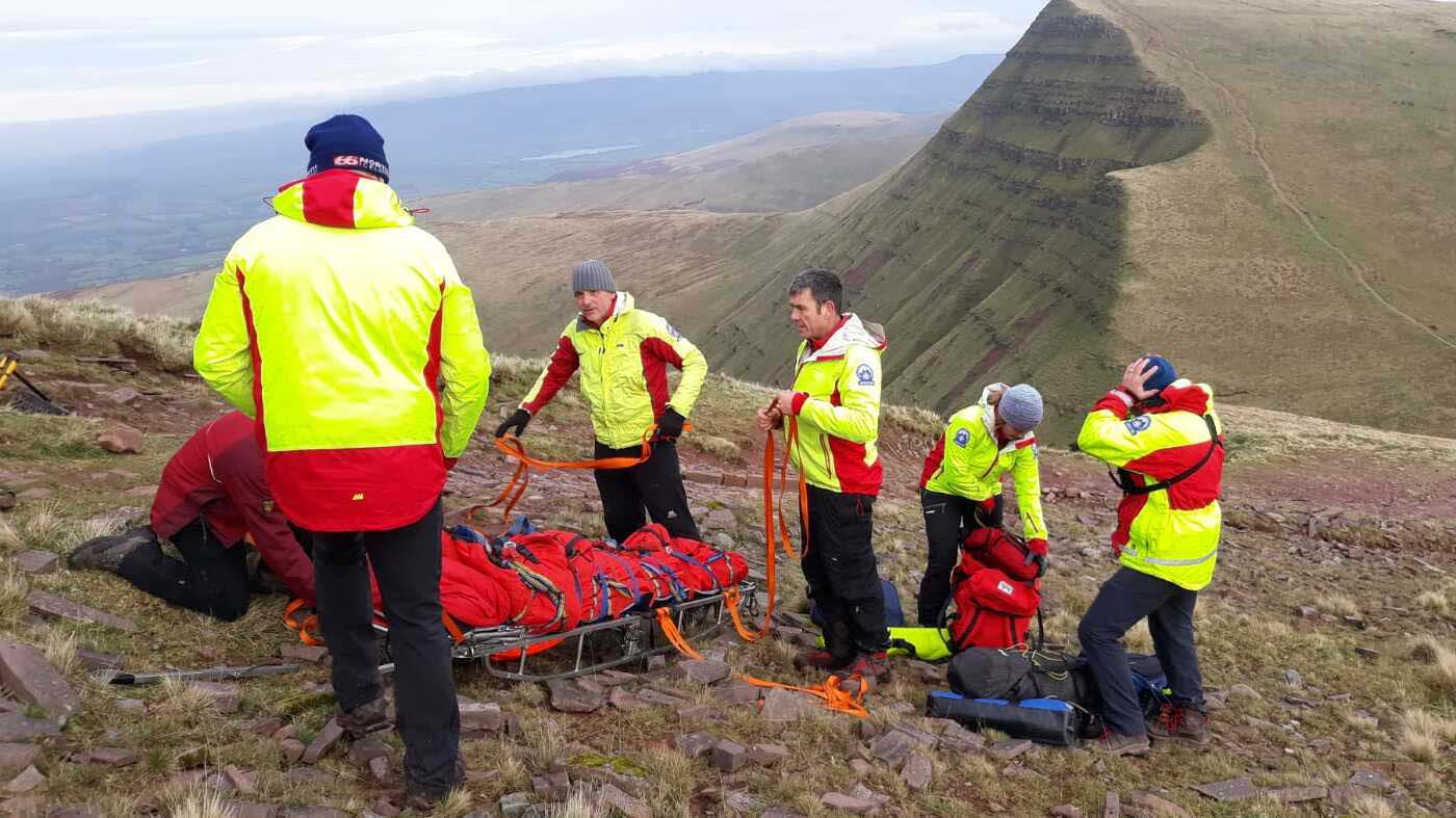 Five members of the Brecon Mountain Rescue Team are dressed in high-visibility gear and surrounded by rescue equipment