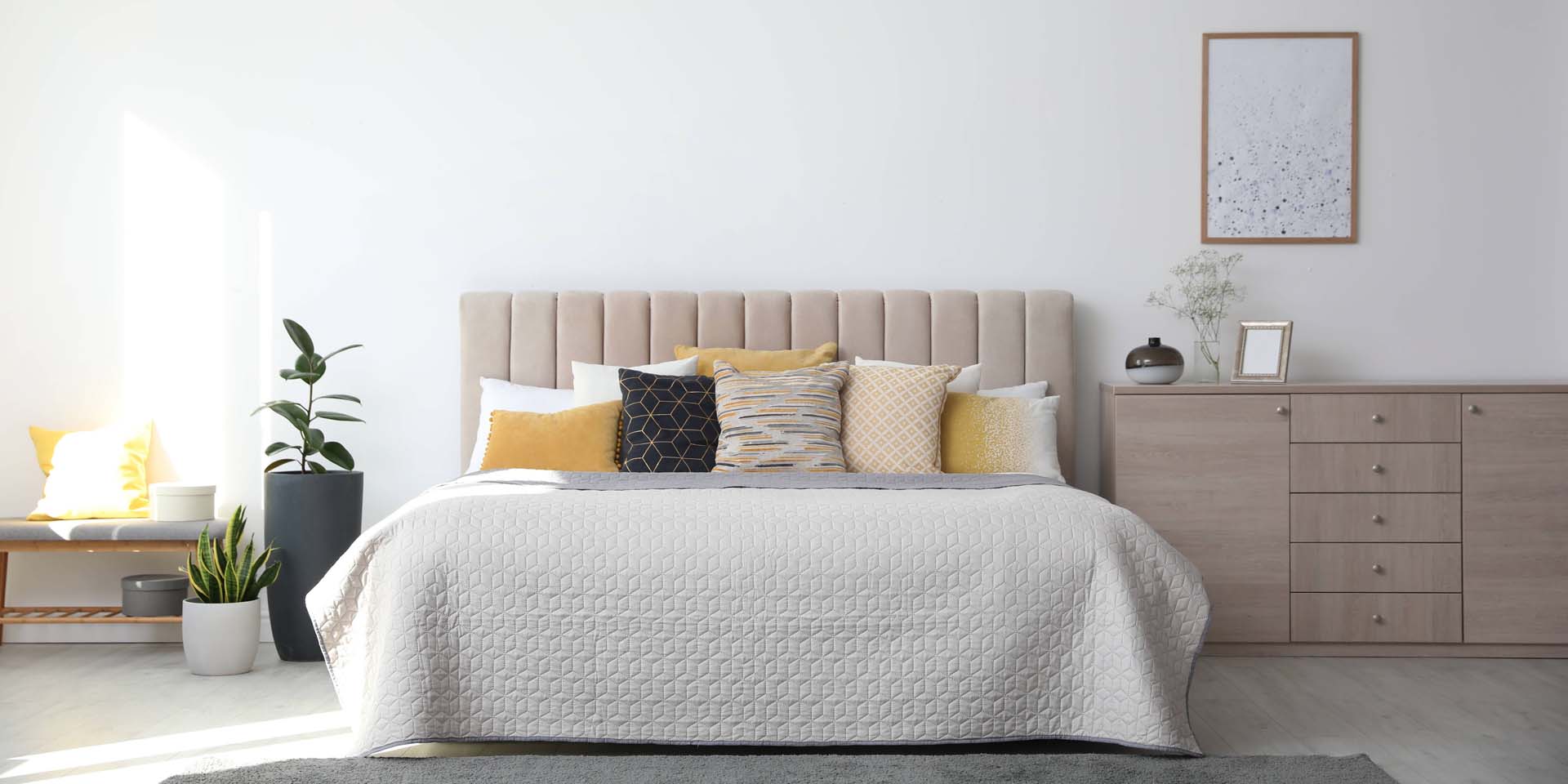 A bedroom in neutral, calming shades with a large bed, soft furnishings and pale wood bedside furniture
