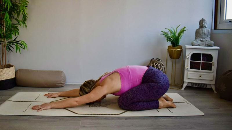 Woman on yoga mat in child's pose - kneeling, with her forehead resting on the floor, arms over her head, resting on the mat - illustrating the best beginner yoga poses