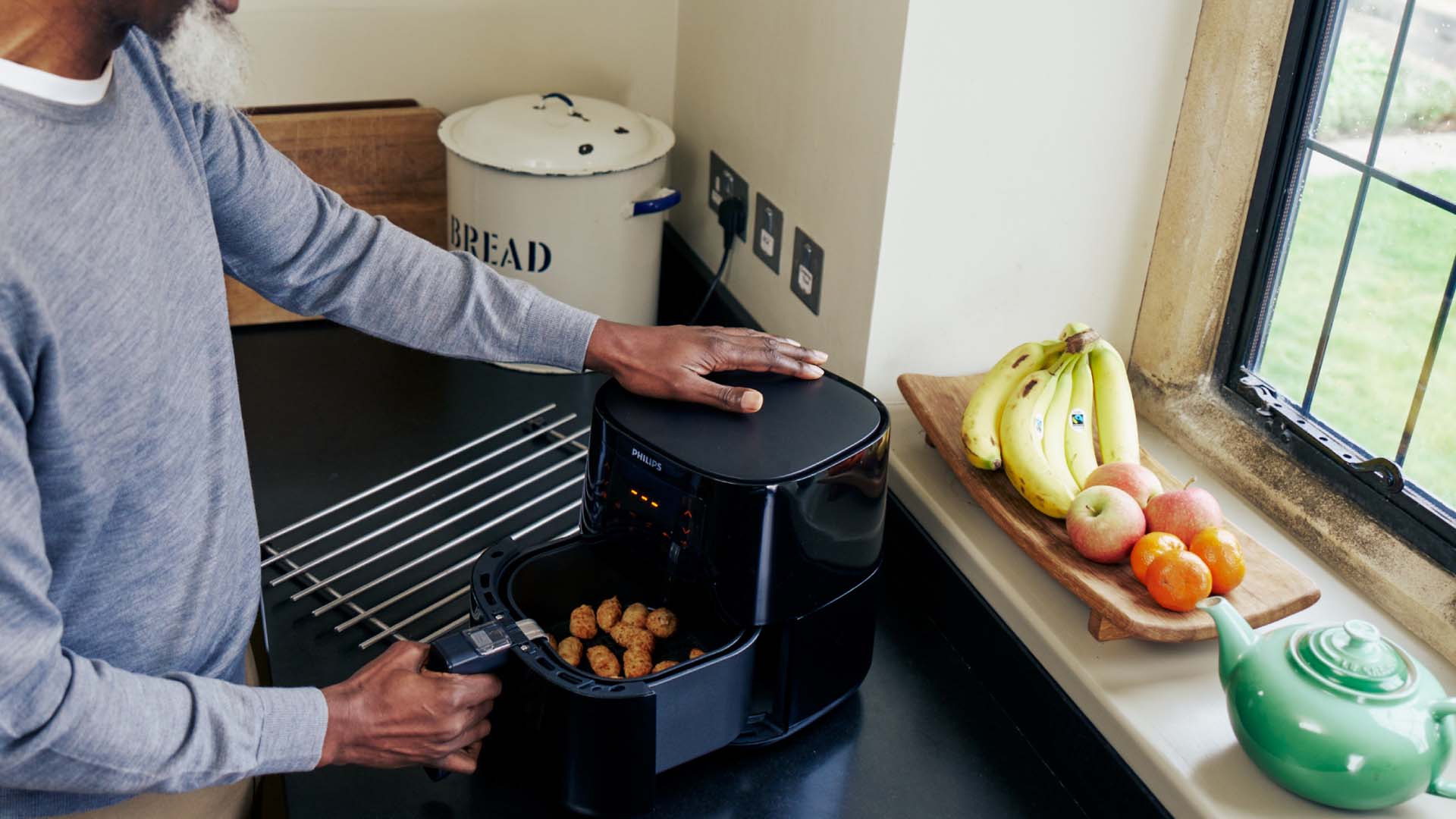 A man opening the air fryer drawer to shake the food part way through cooking