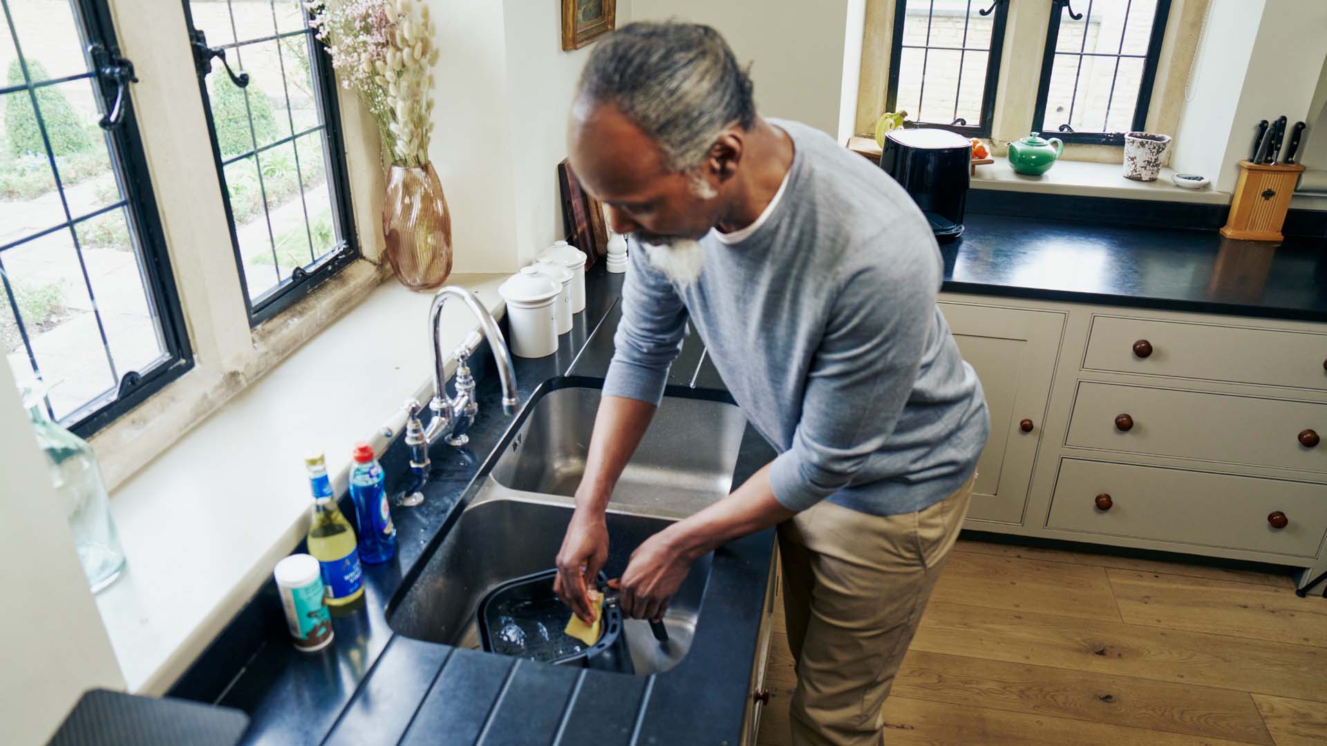 A man washes the drawer of an air fryer in the sink