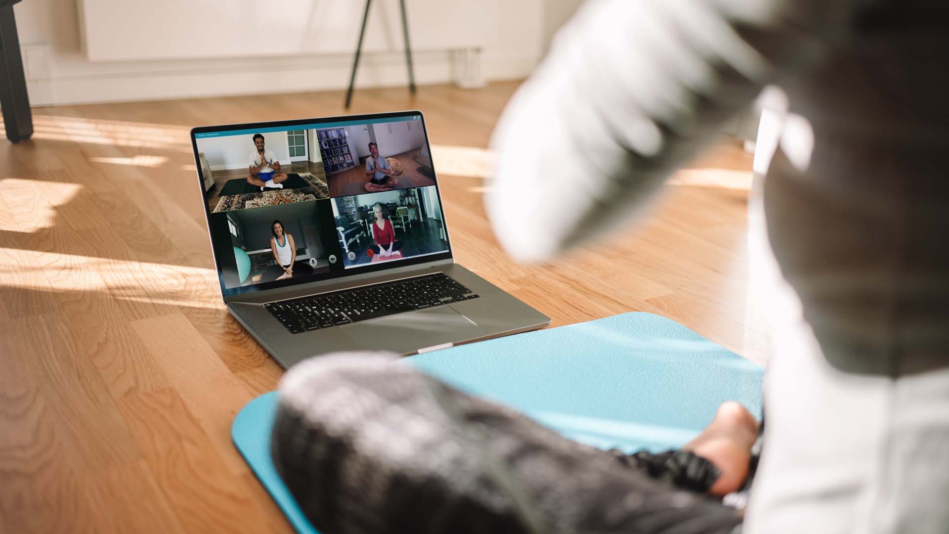 A person participating in an online exercise class; sitting cross-legged on an exercise mat with a laptop open in front of them