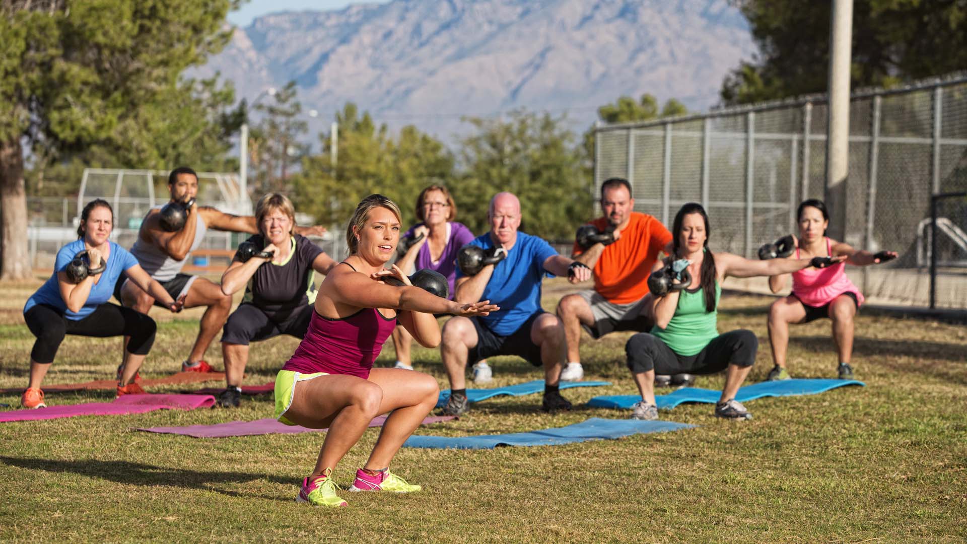 A large group of people performing a squat in an outdoor exercise class