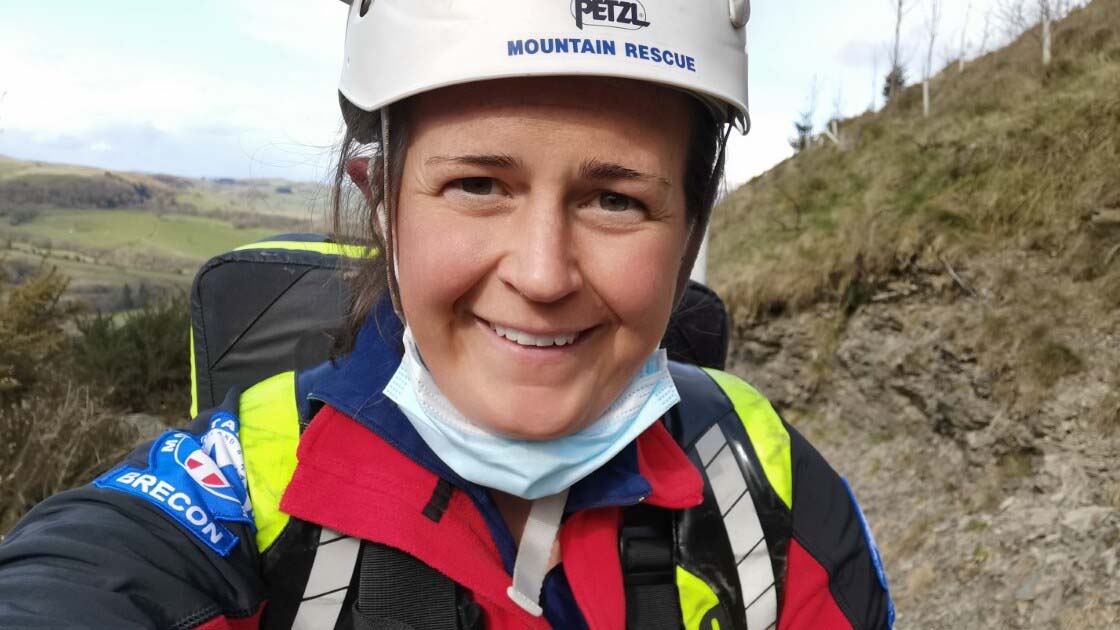 A member of the Brecon Mountain Rescue Team in brightly accented hiking gear and a white helmet