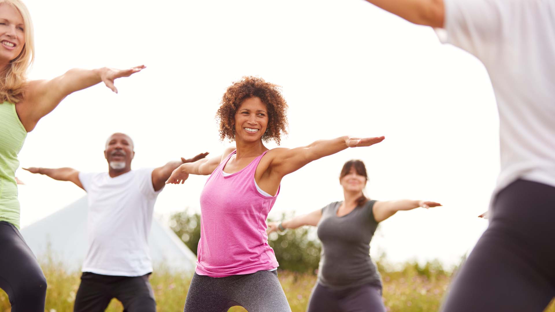 A group of people practising yoga poses outdoors; warrior two yoga pose