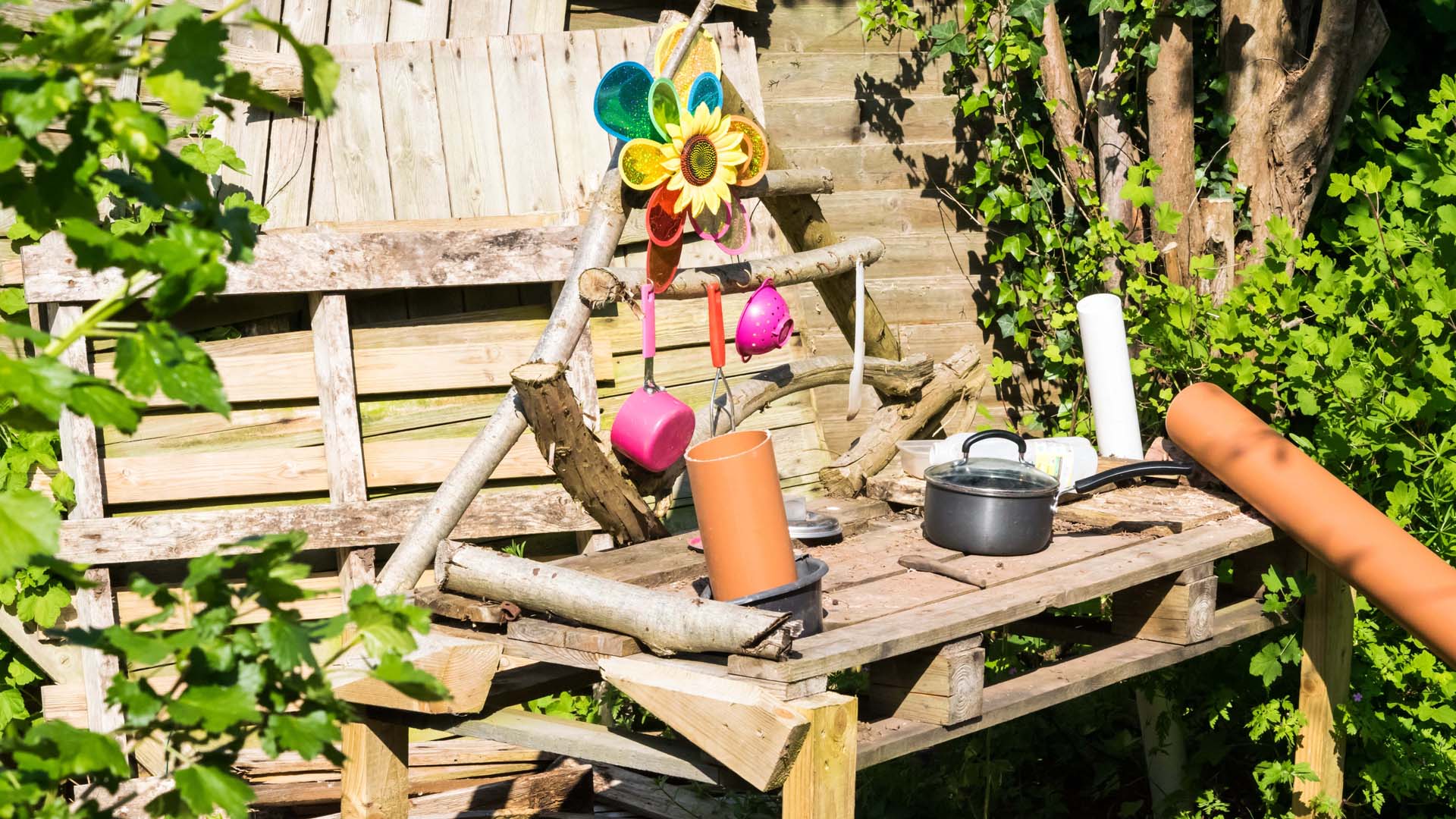 A handmade mud kitchen built from wood and decorated with pots and pans for children to play with.