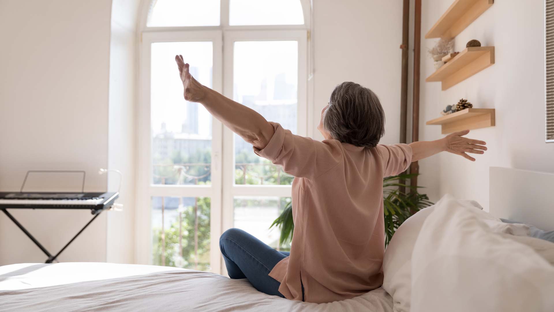 A woman sitting on a bed and stretching her arms to greet the day