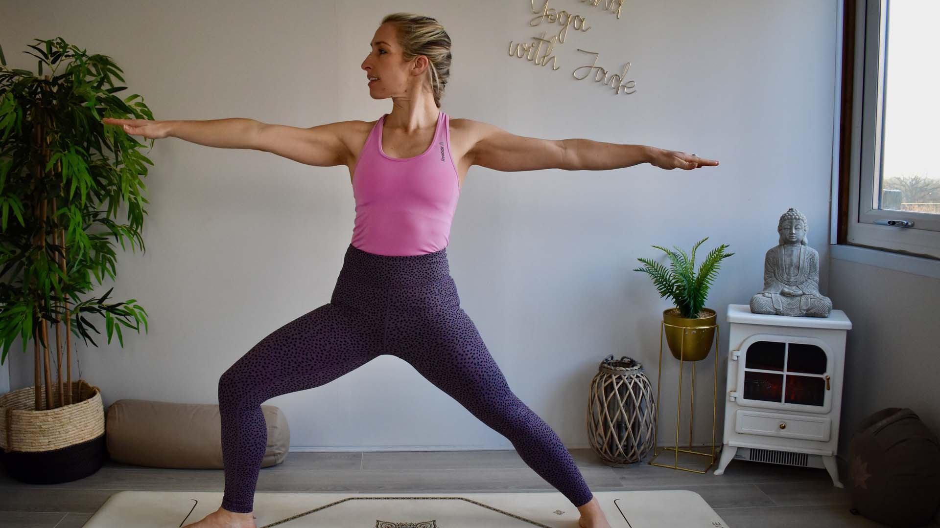 A woman on a yoga mat in Warrior Two stance.