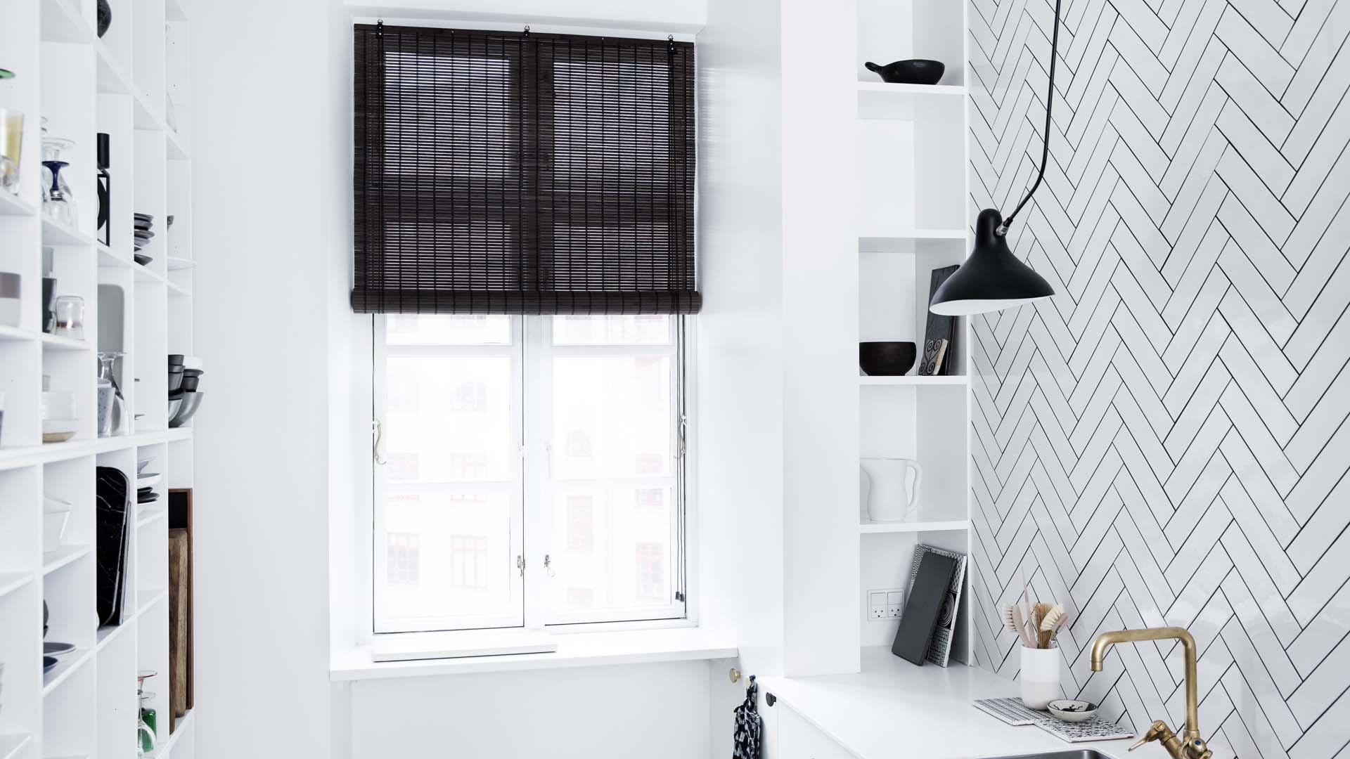 A small kitchen with a statement wall of geometric grey tiles and a window with a black blind