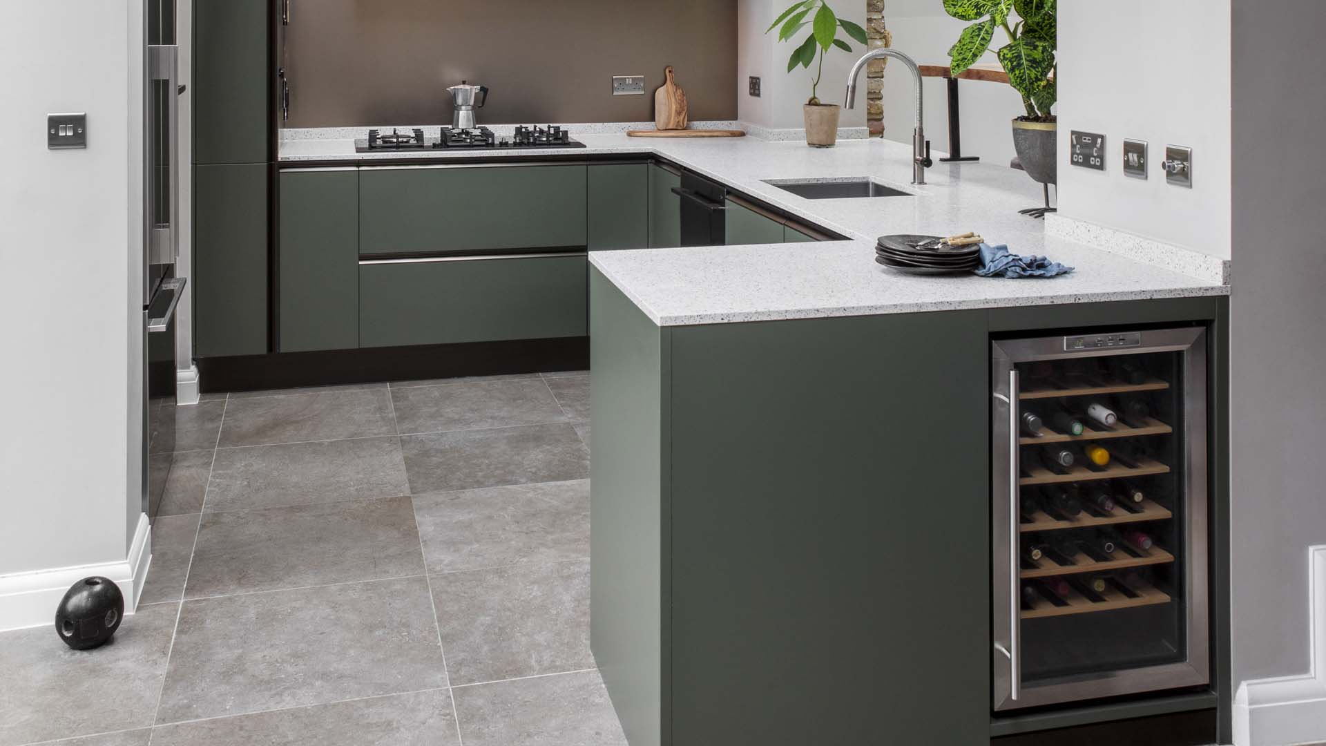 A sage green kitchen with white counters and large grey floor tiles