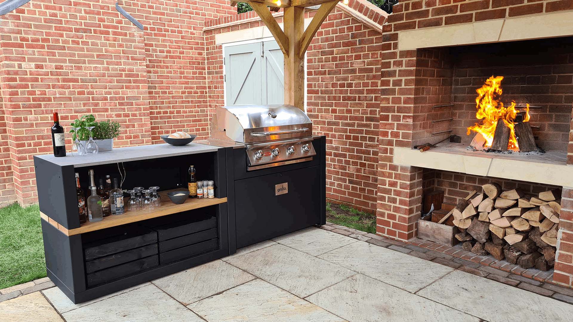 A modern outdoor kitchen unit with BBQ next to a wood burning fire