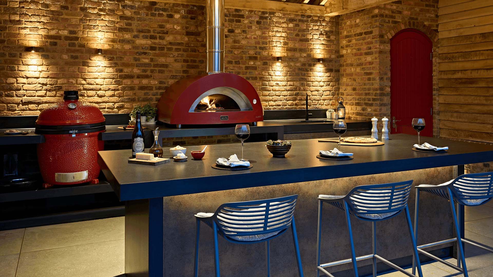 Completely covered outdoor kitchen with vibrant red barbecue egg and wood-fired pizza oven backing onto face brick walls