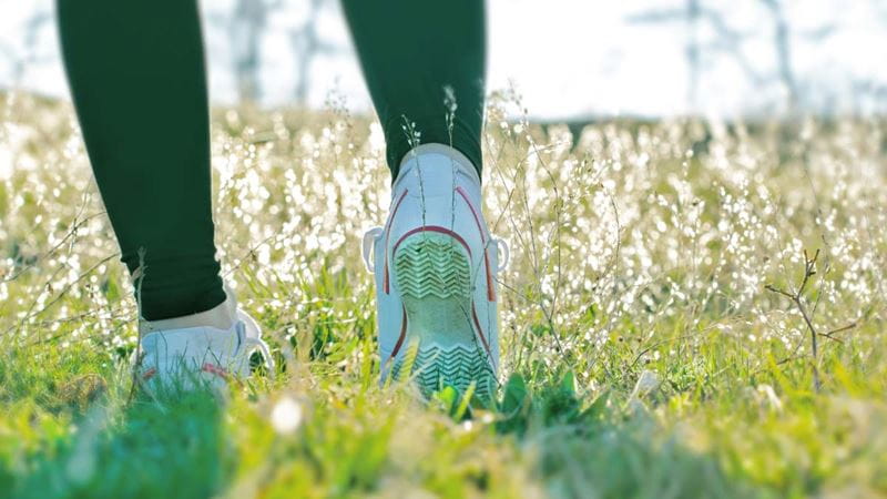A pair of feet in trainers walk through a grassy field