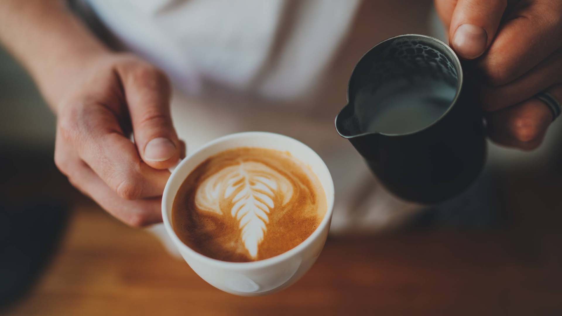 Close-up of a barista making a cappuccino with latte art.