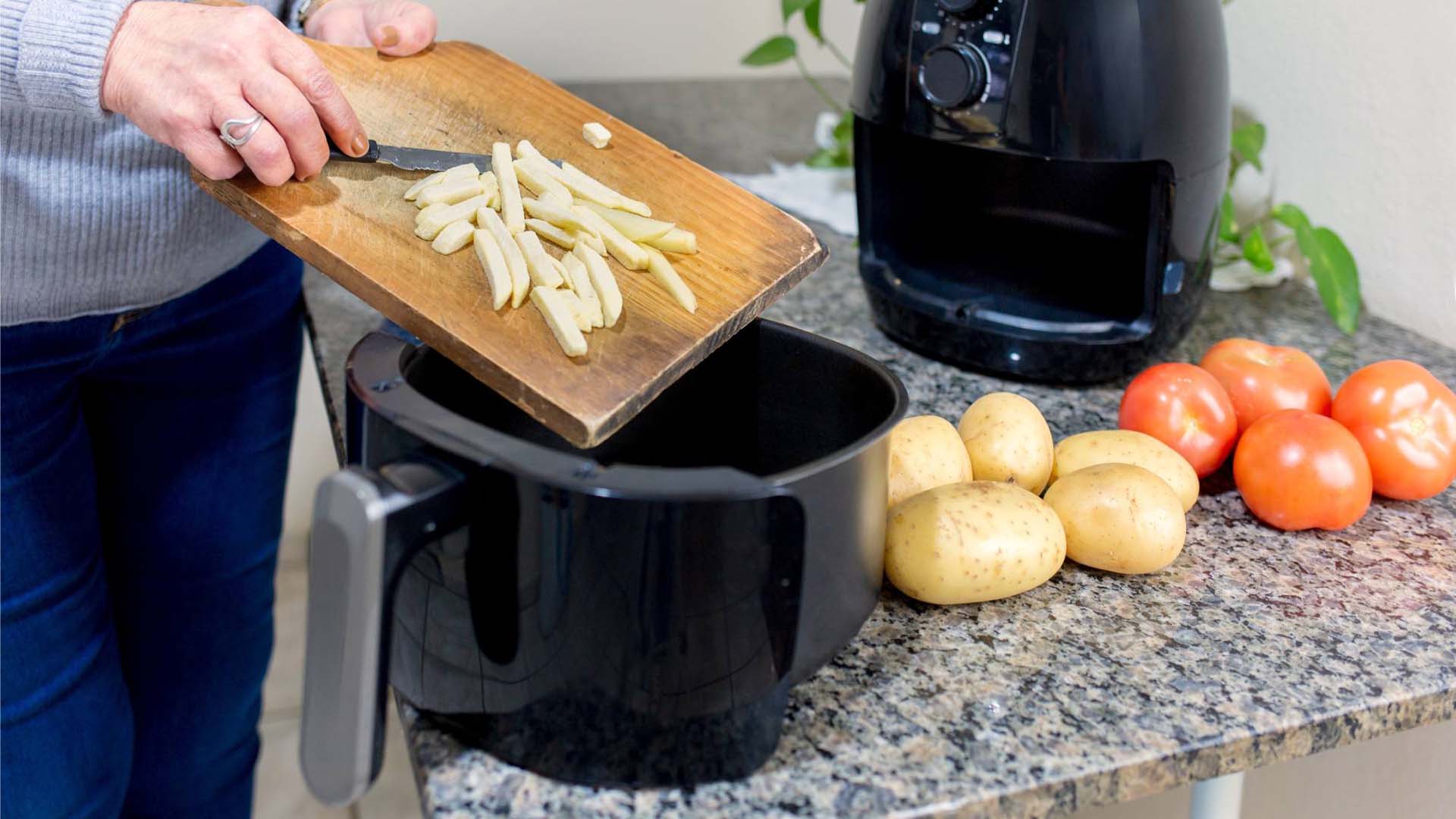 A person putting chopped potatoes into an air fryer