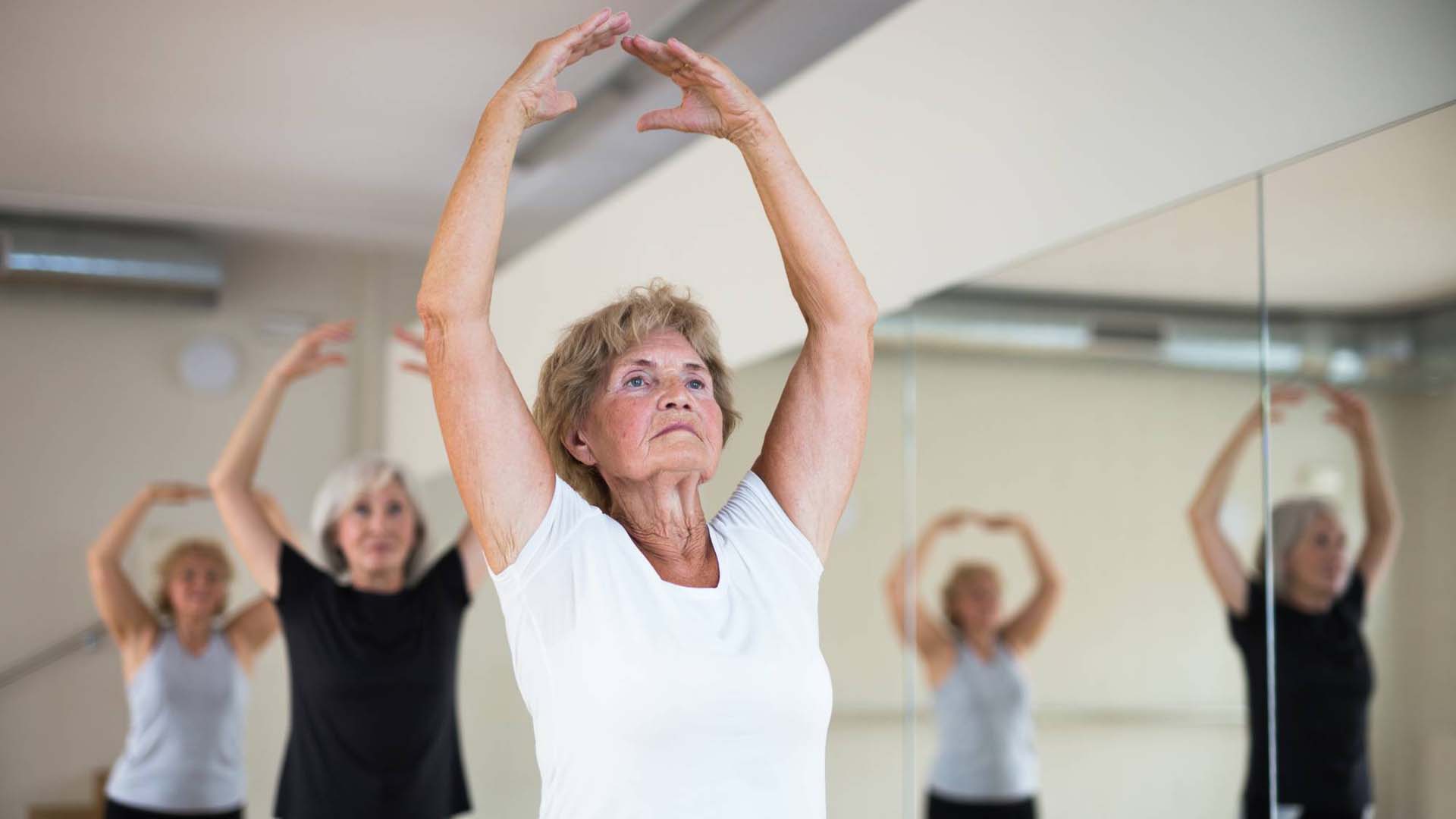 Three older women doing a ballet exercise class in a workout studio