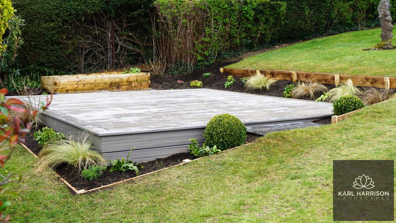 A sloping lawn with a raised flat deck surrounded by a planted border.