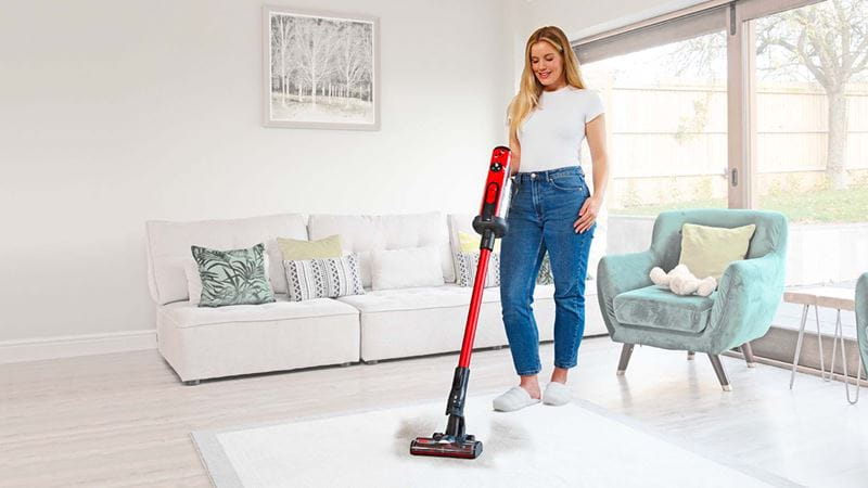 A woman using a cordless Henry vacuum in a living room decorated in neutral shades