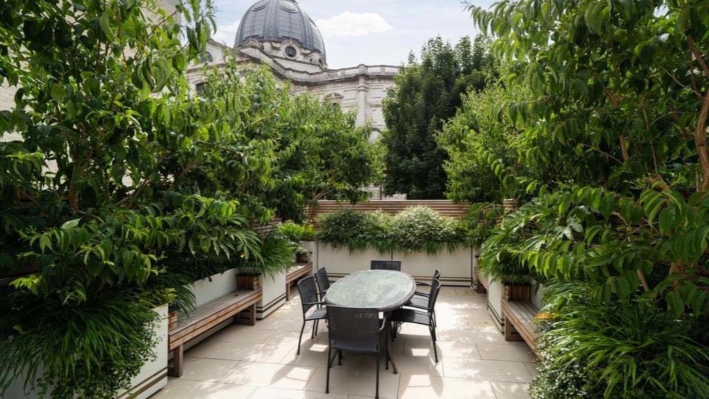 Small city house outside area with a black oval table and chairs, surrounded by integrate benches between the planters