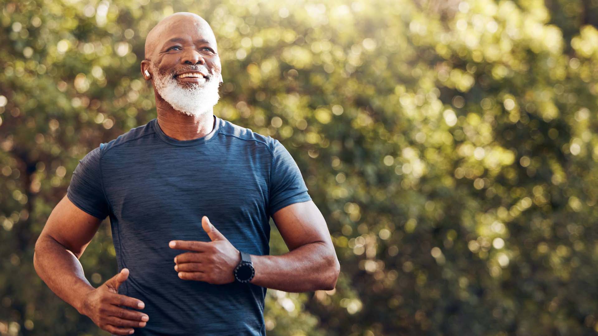 Happy black man running in park with music, smile and mockup in nature, garden and workout. Senior male, outdoor runner and motivation for fitness, energy and healthy exercise training with earphones