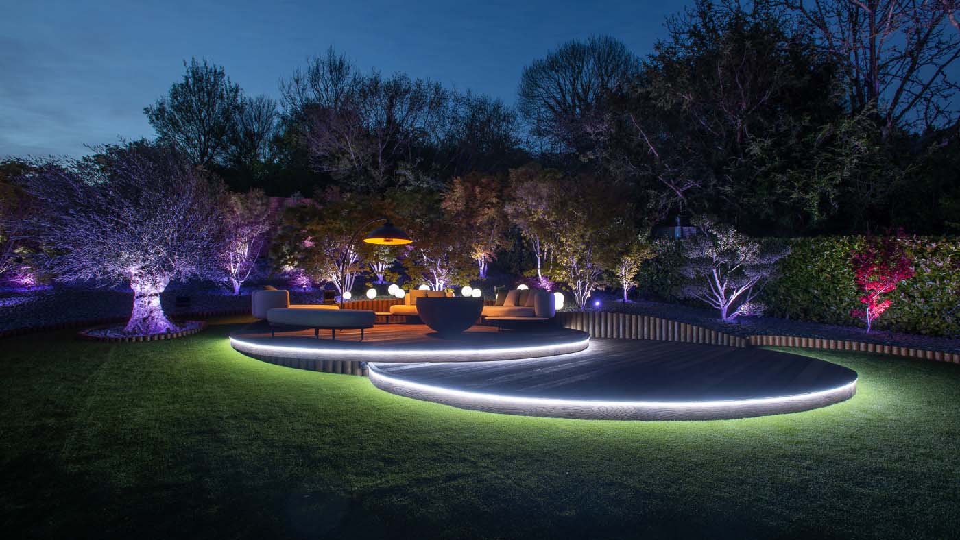 Two circular decked areas in a garden with up-lighting around the base of the decking and surrounding trees.