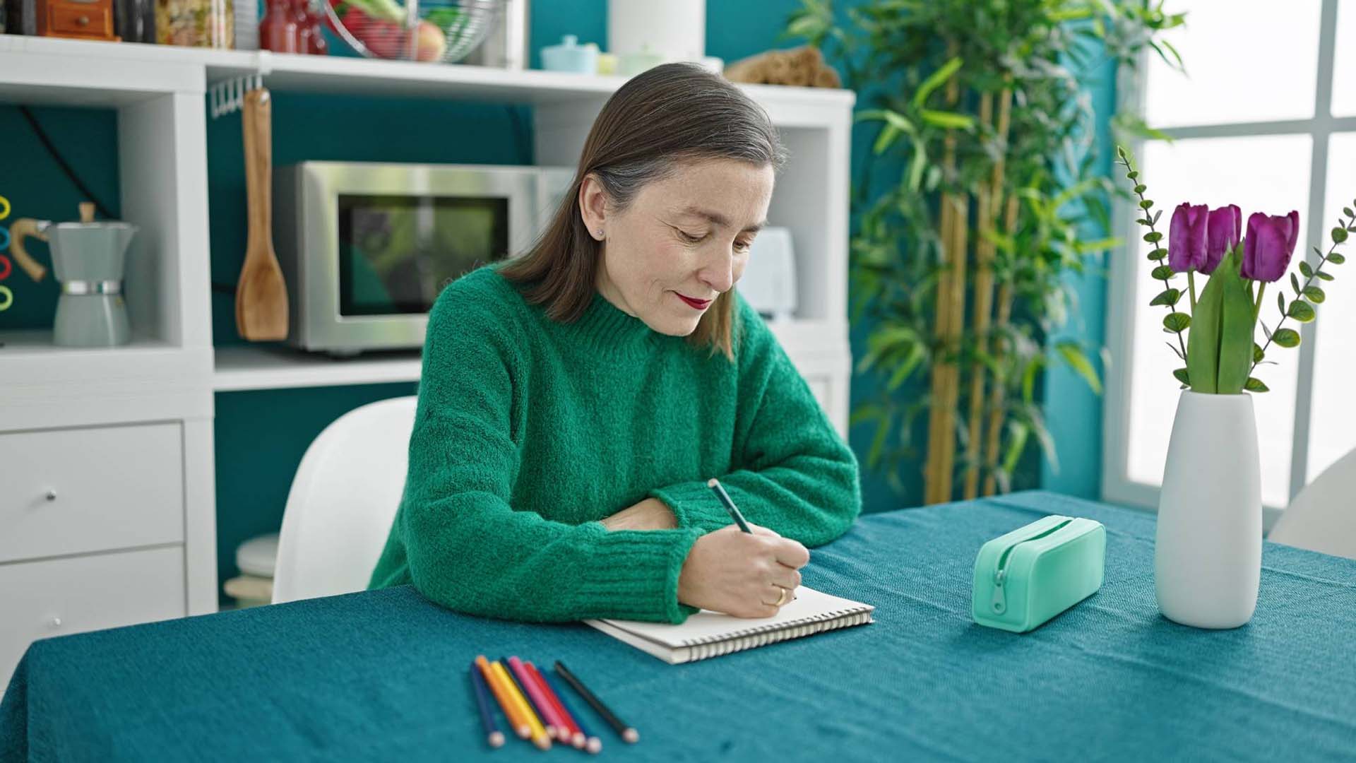 Mature hispanic woman with grey hair sitting painting with color pencils at dinning room