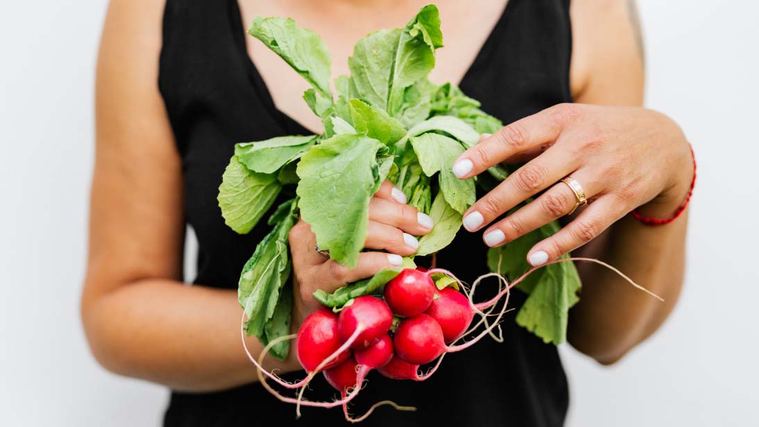 a woman holding a bunch of radishes