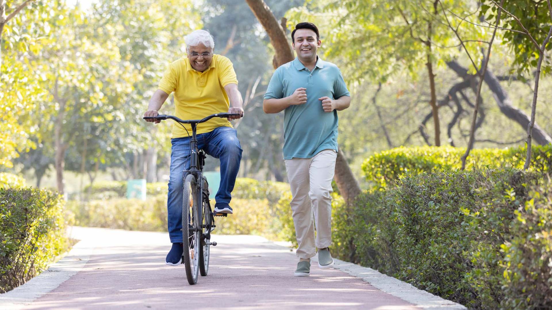 Cheerful senior man riding bicycle  while son running at park
