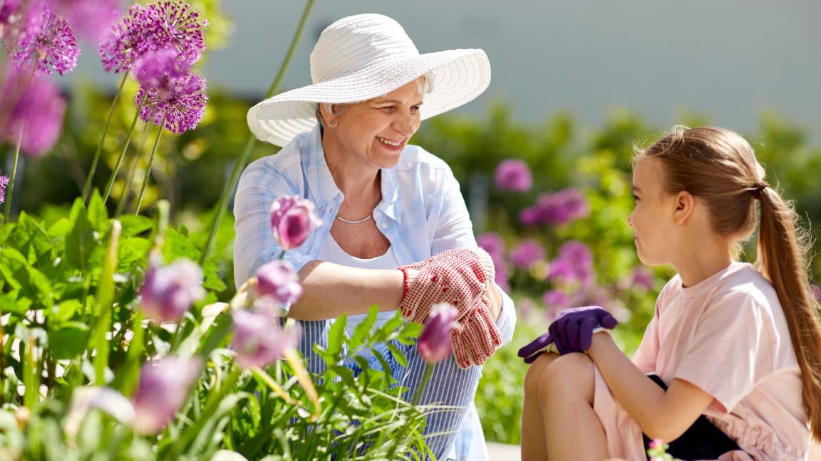 Happy grandmother and granddaughter with flowers at summer garden