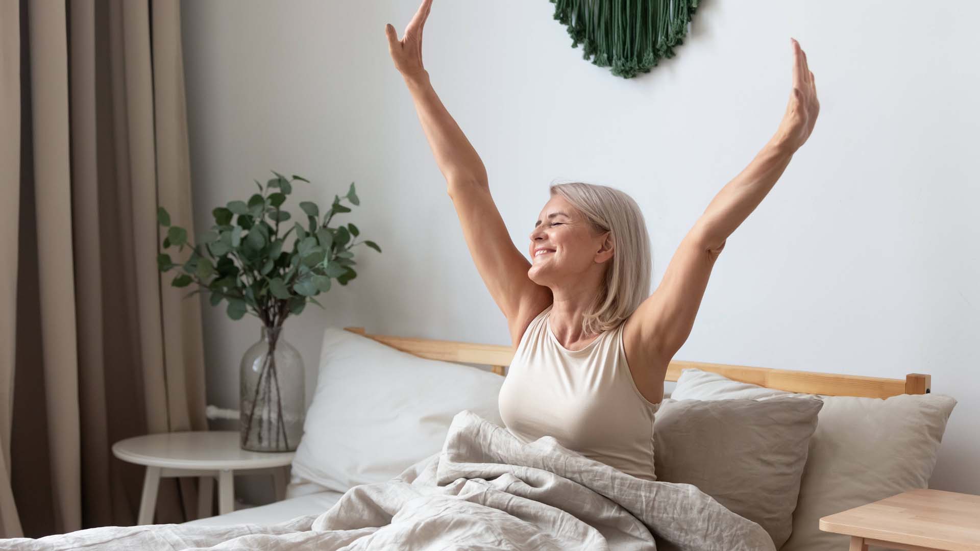 woman in bed reaching upwards feeling good