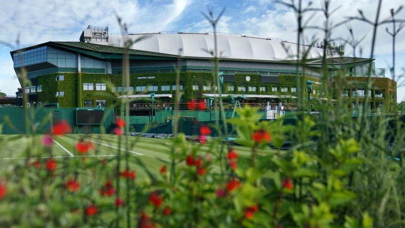 A view through the flowers behind Court 8 looking towards Centre Court ahead of The Championships 2022. Held at The All England Lawn Tennis Club, Wimbledon. Day -18 Thursday 09/06/2022. Credit: AELTC/Chloe Knott.
