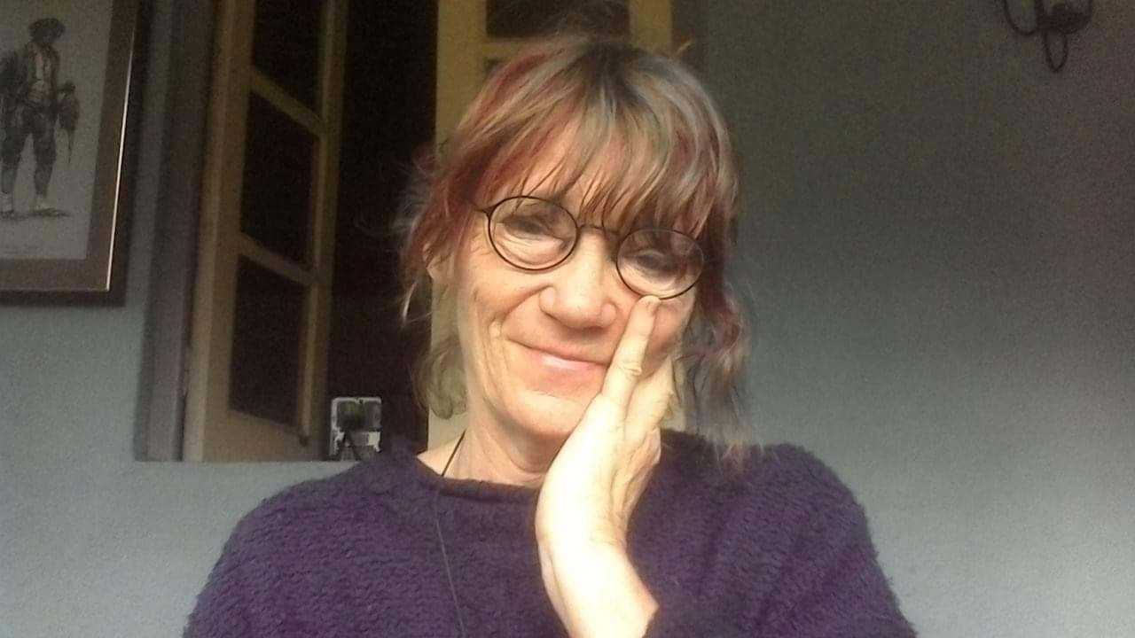 The head and shoulders of a smiling middle-aged woman with curly brown hair tied up and glasses.