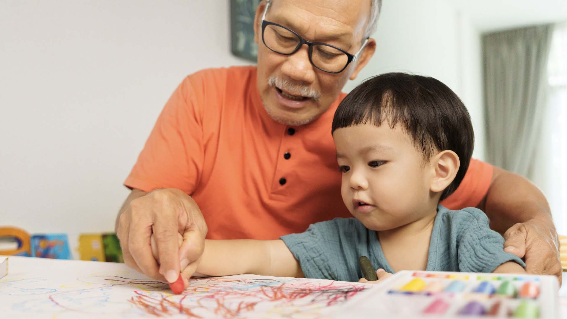 An older man and a small boy sitting at a table colouring with crayons