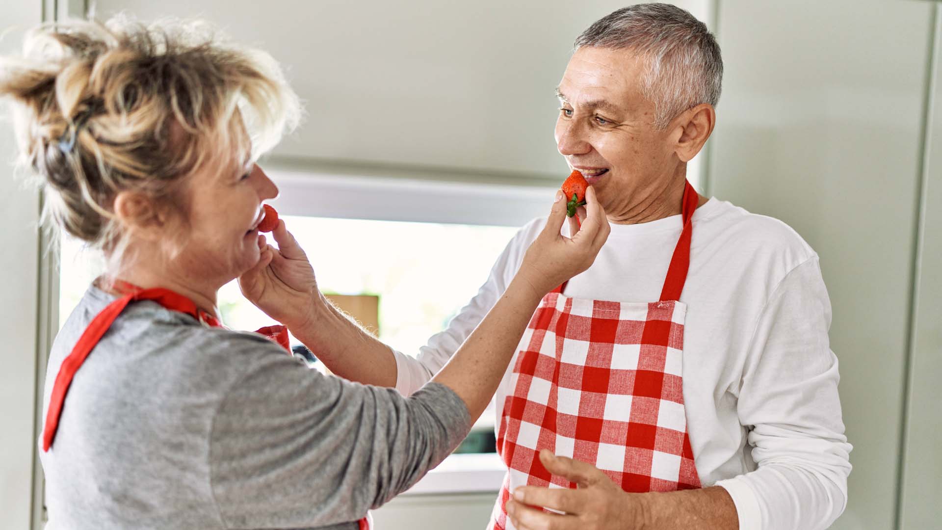 A man and woman eating strawberries, both wearing red and white aprons
