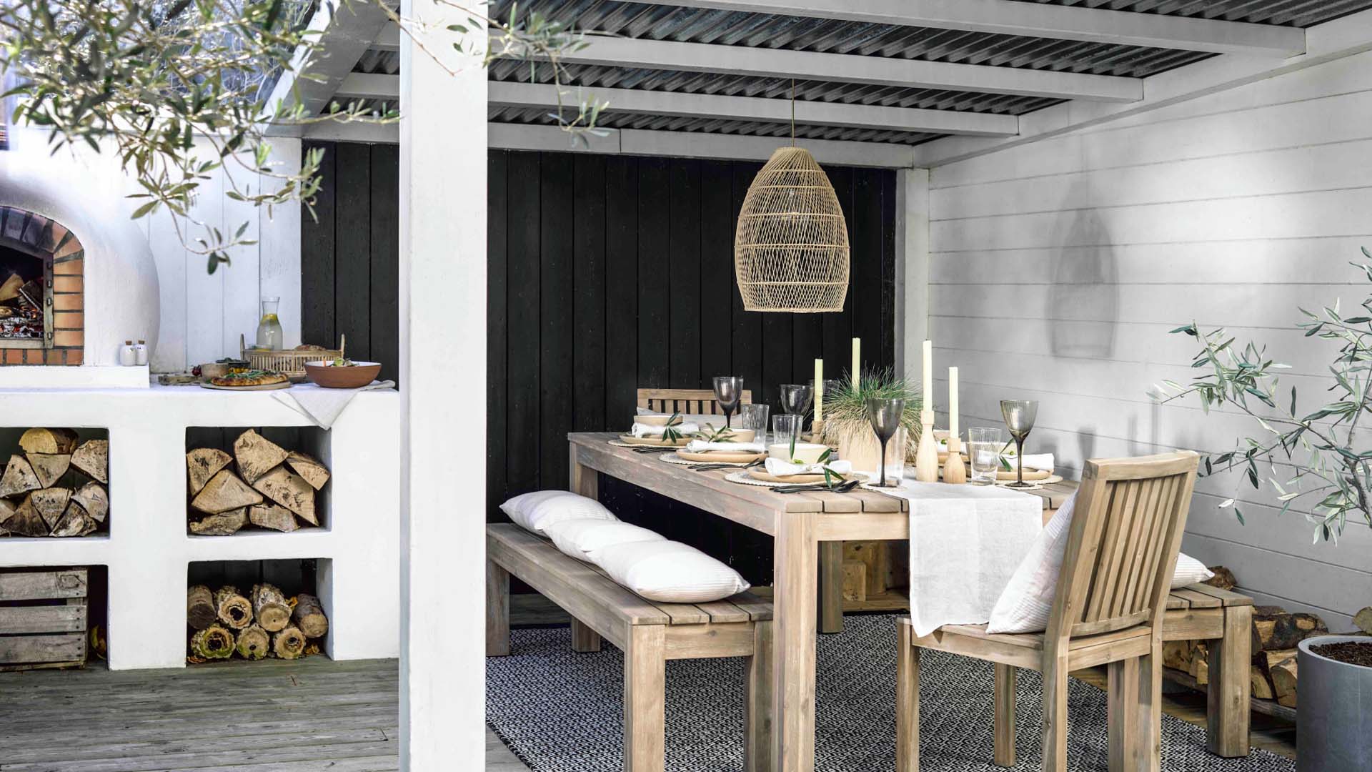 White Pergola patio corner design, near an outside wood-burn pizza stove with a long wood dinner table, two chairs, and two long benches