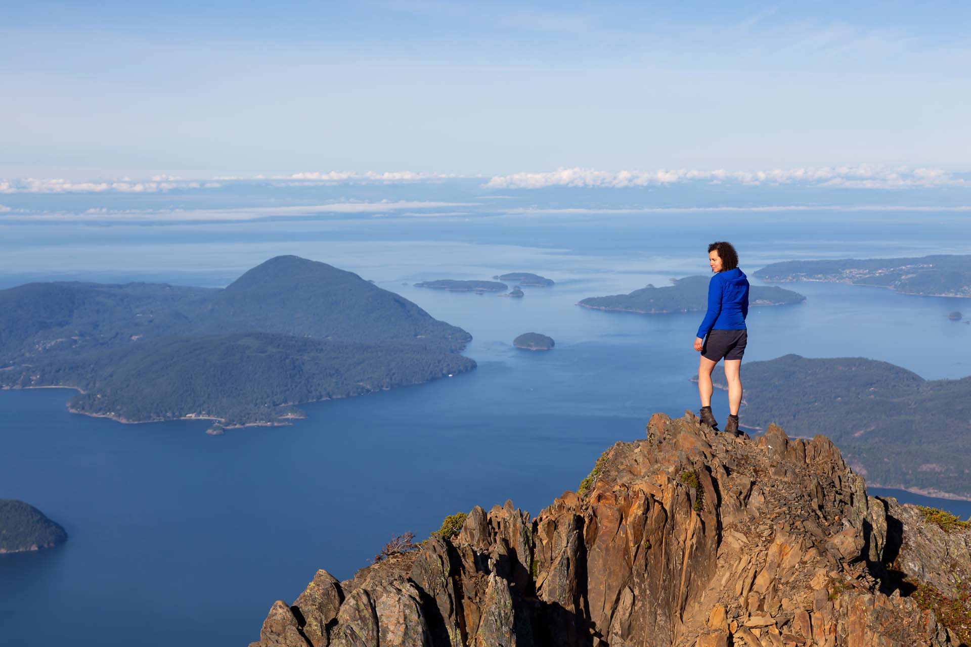 A hiker stands on a mountain peak gazing out at his surroundings