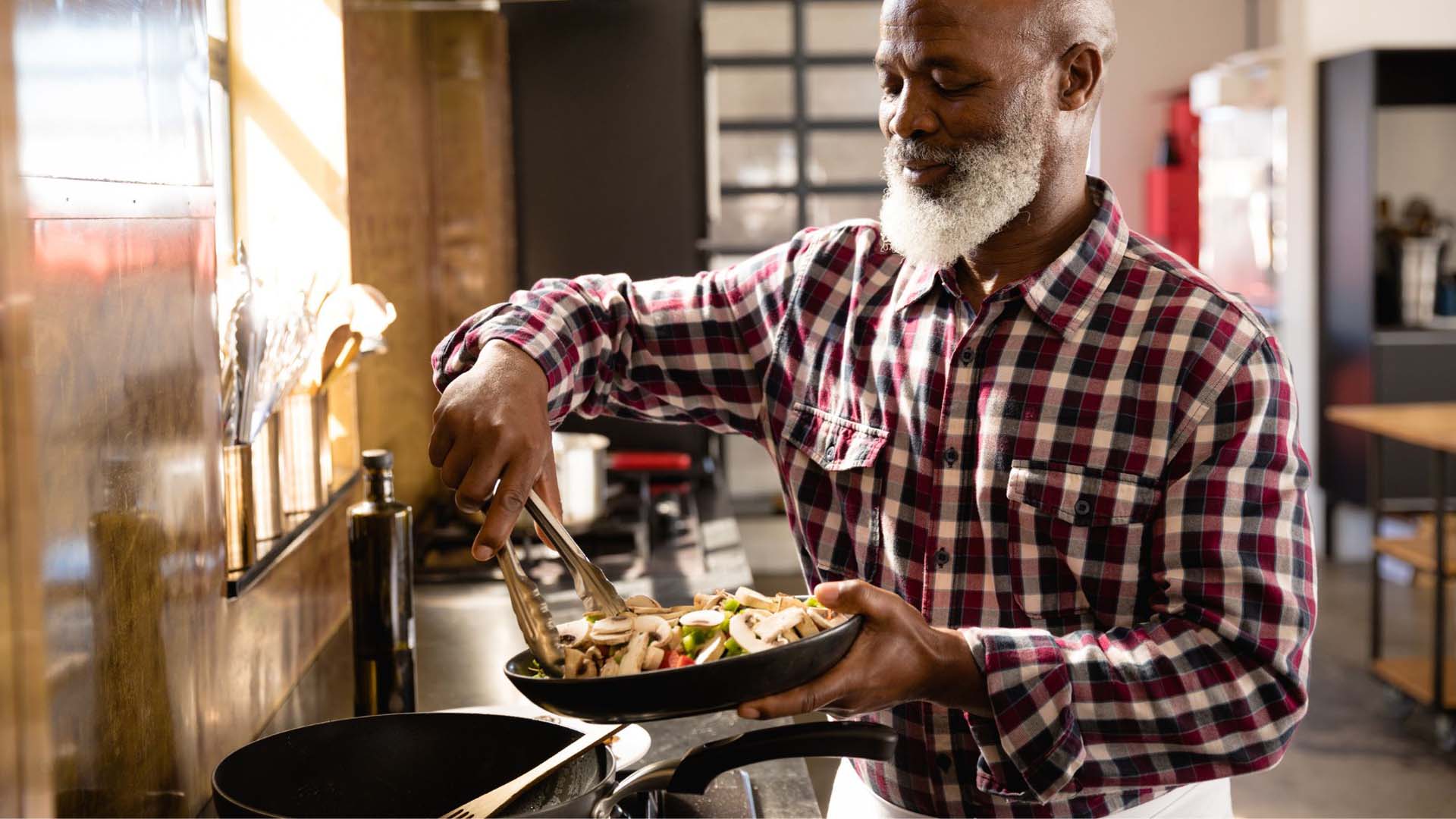 An older man adding raw vegetables to a pan on the hob