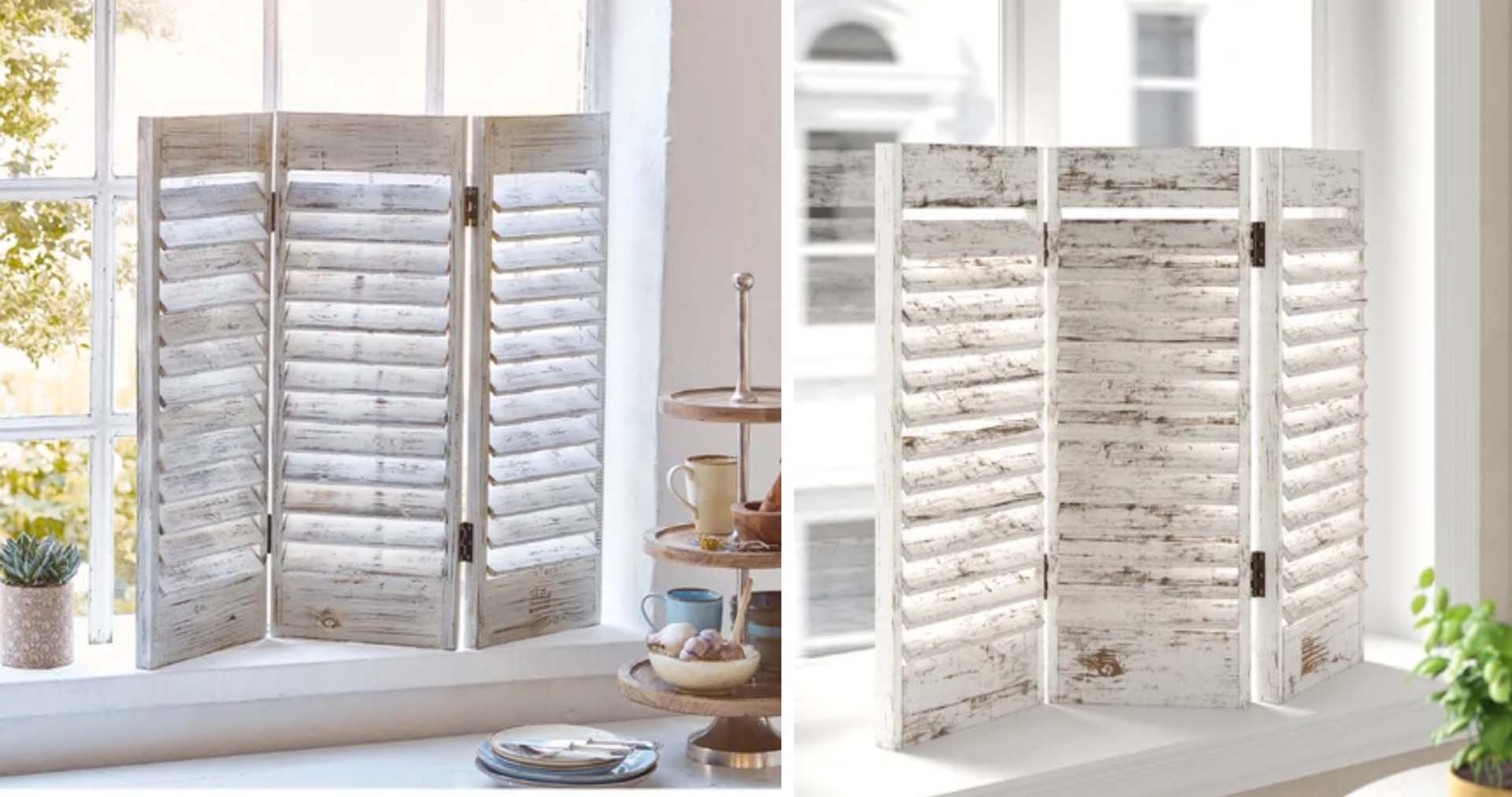 A small slatted window screen in a shabby chic style standing on a window sill