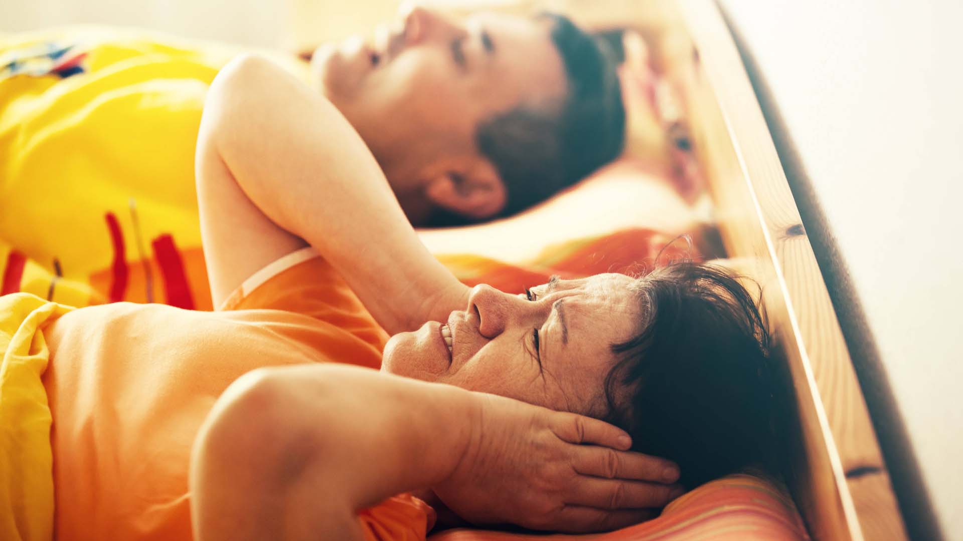 Couple lying in bed, woman has hands over ears