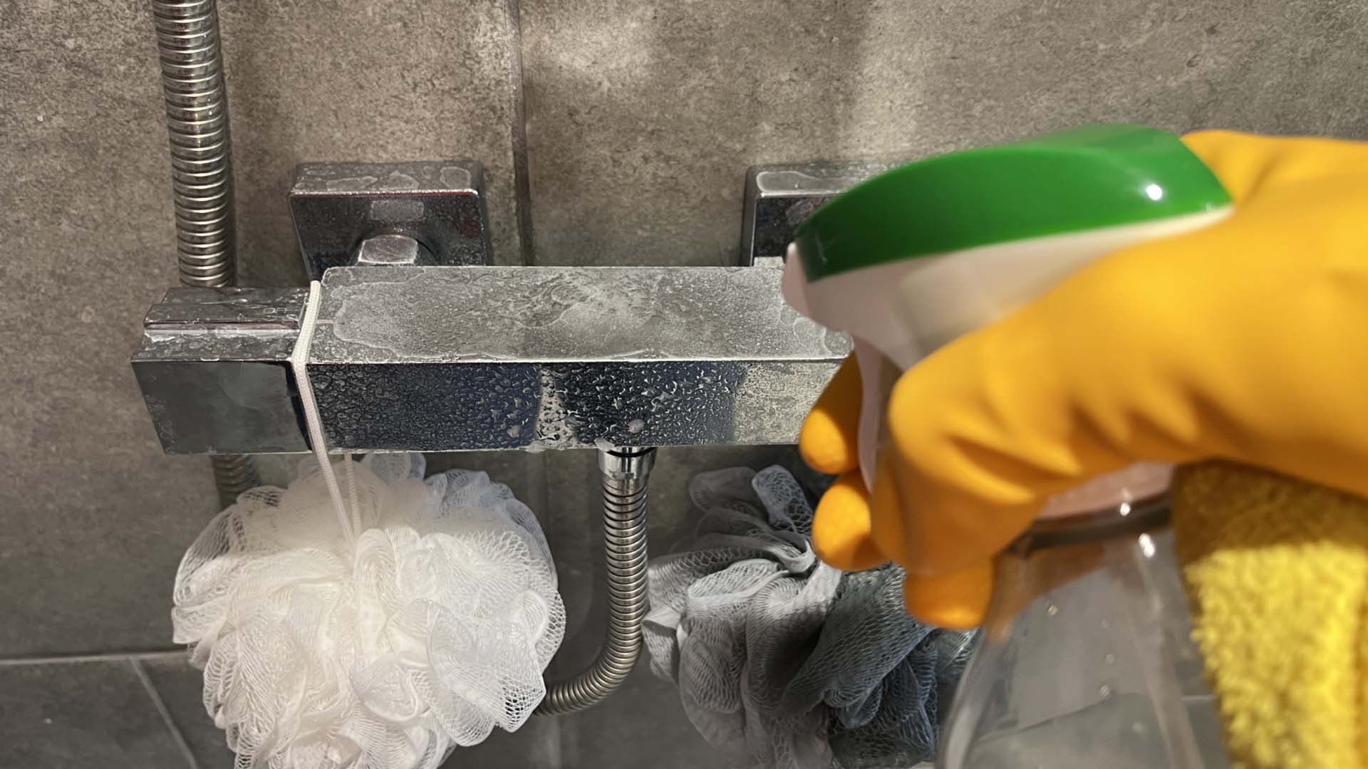A hand in a cleaning glove spraying a shower to clean it